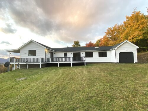 A white house with a black roof is sitting on top of a grassy hill.