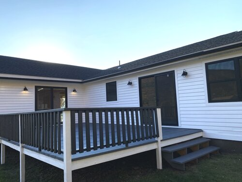 A white house with a black deck and stairs in front of it.