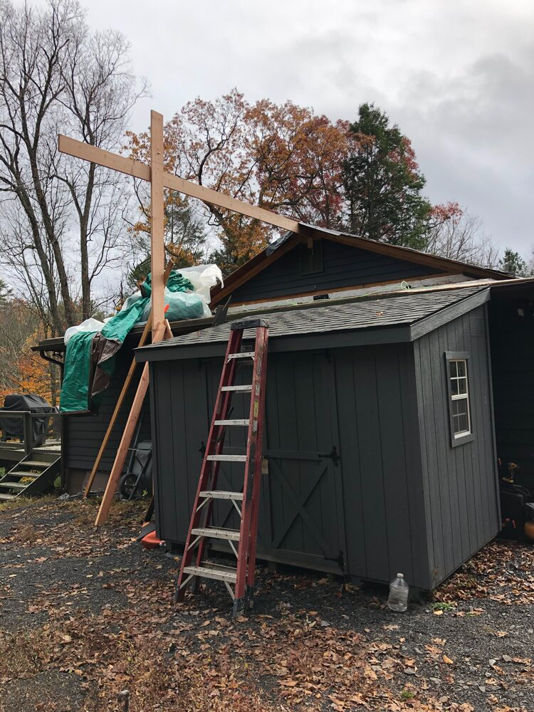 A ladder is sitting next to a shed with a cross on top of it.