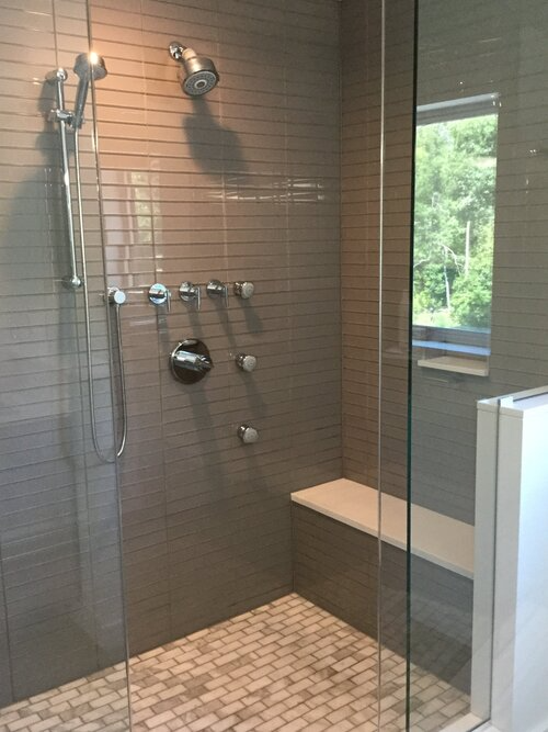 A walk in shower with a glass door and a bench.