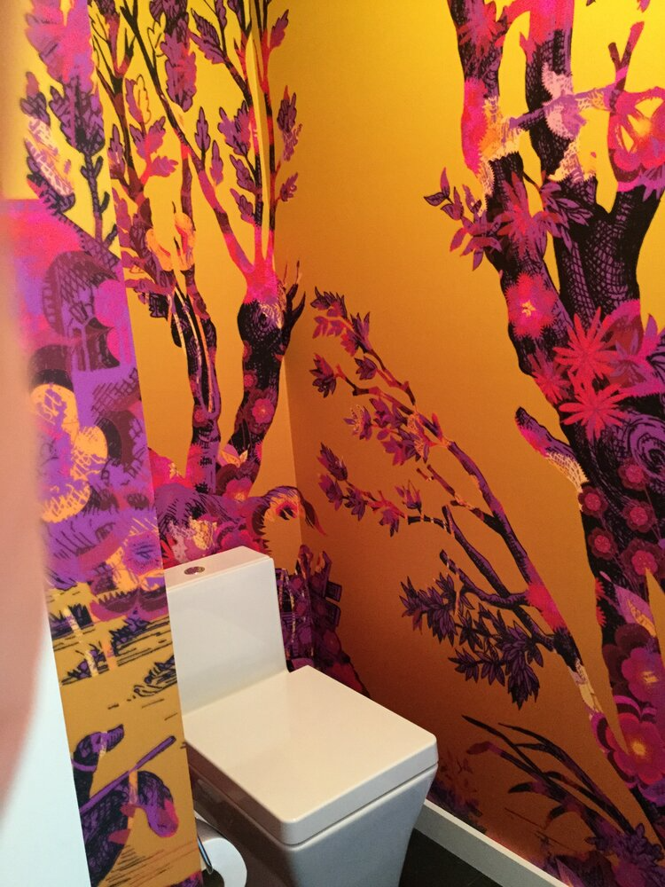 A toilet in a bathroom with a mural on the wall
