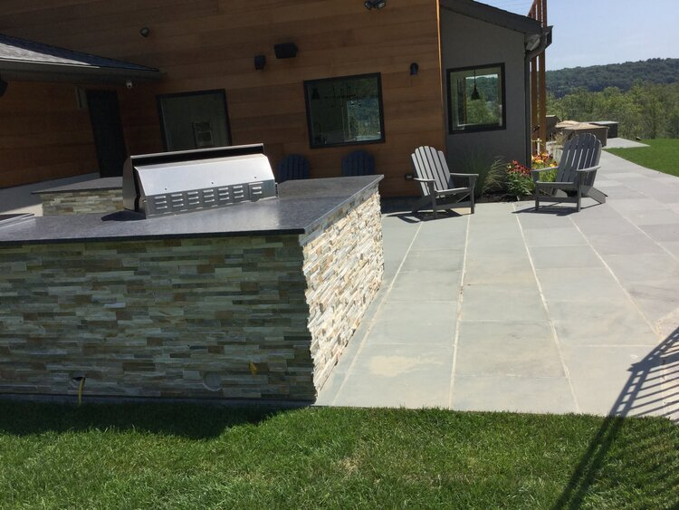 A patio with a grill and chairs in front of a house.