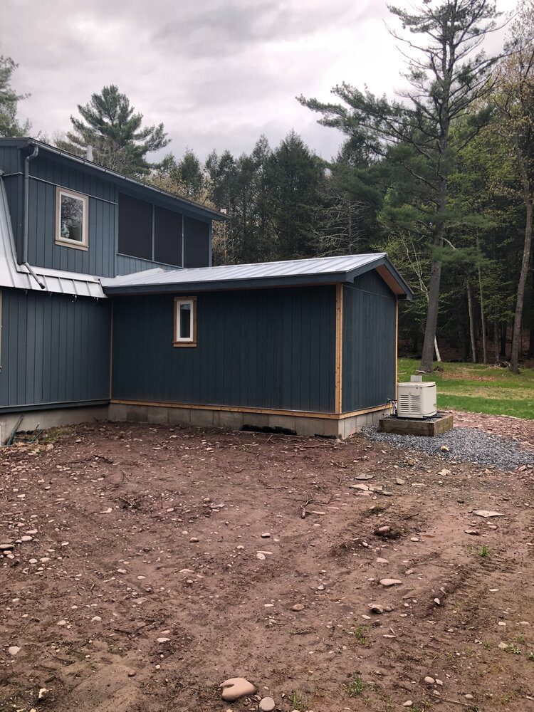 A blue house with a screened in porch is sitting in the middle of a dirt field.