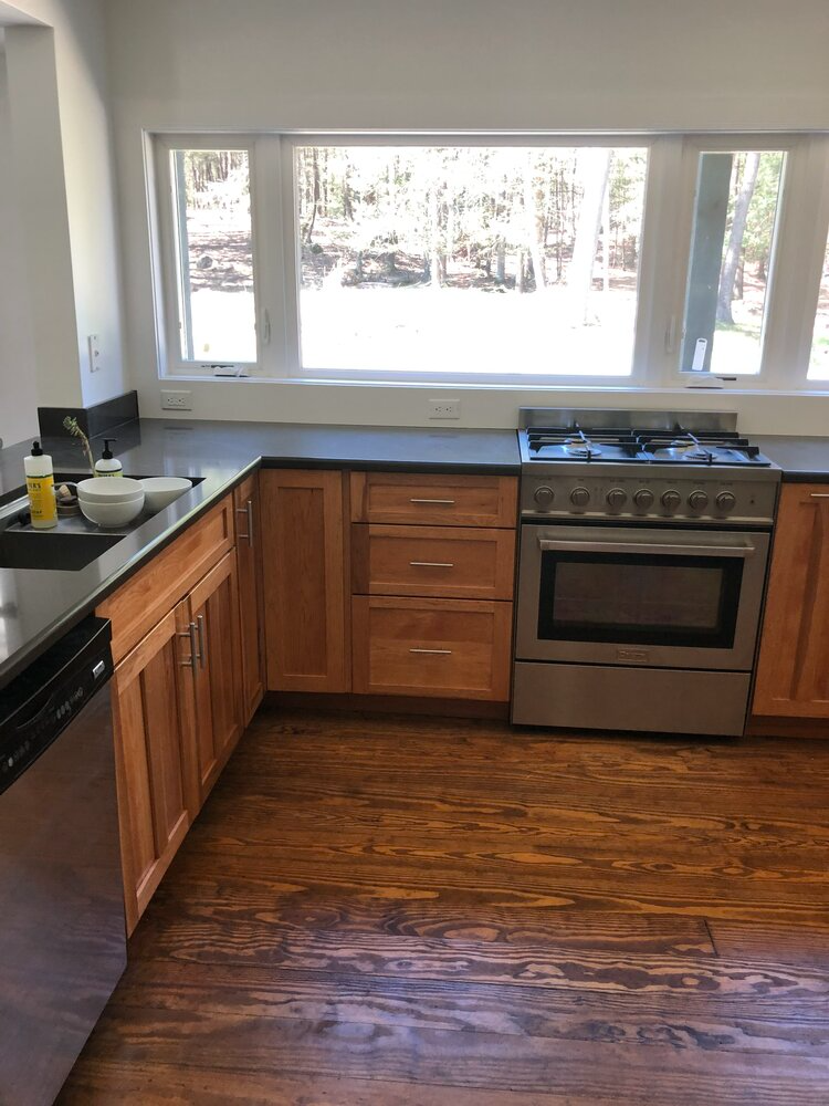 A kitchen with wooden cabinets , a stove , a sink , and a window.