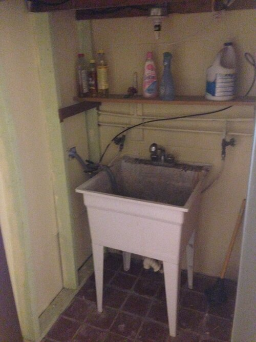 A white laundry sink is sitting in a corner of a room.