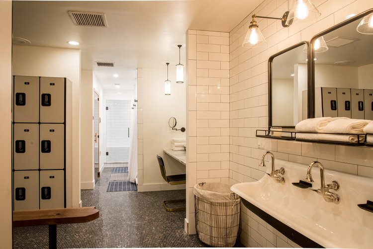 A bathroom with two sinks , two mirrors and lockers.