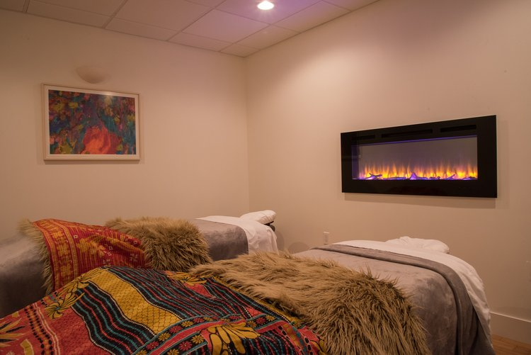 There are two beds in a room with a fireplace.