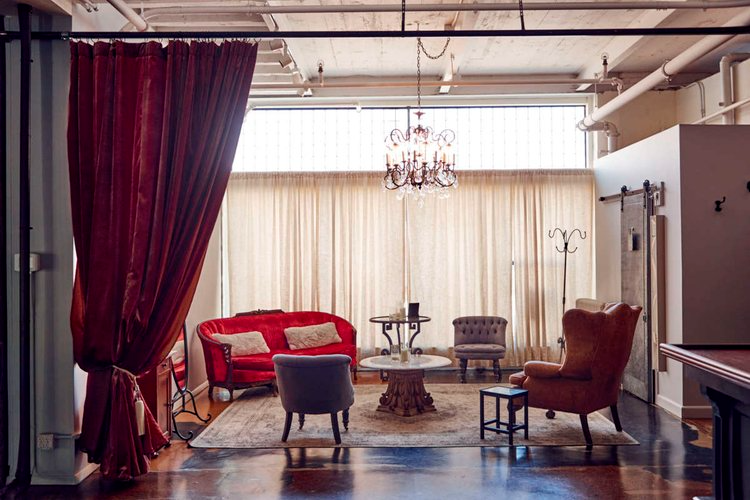 A living room with a red couch , chairs , a table and a chandelier.