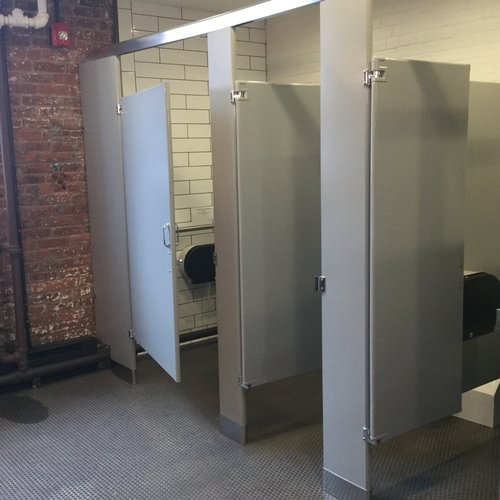 A row of toilet cubicles in a public restroom with a brick wall.