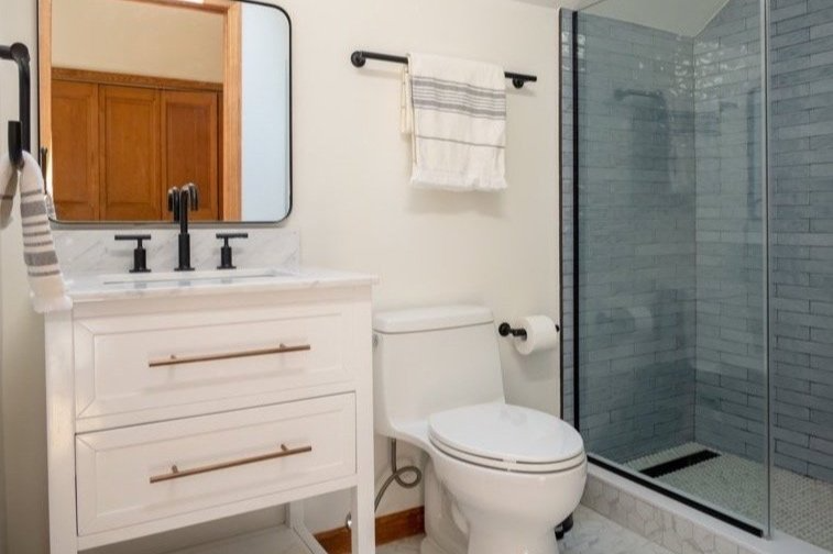 A bathroom with a toilet , sink , mirror and walk in shower.