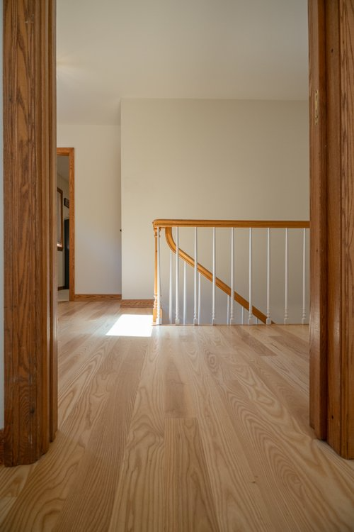A hallway with hardwood floors and a staircase in a house.