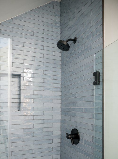 A shower with blue tiles and a black shower head.