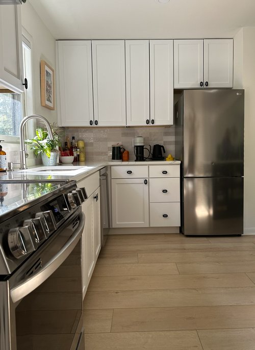 A kitchen with white cabinets , a stove , a refrigerator , and a sink.