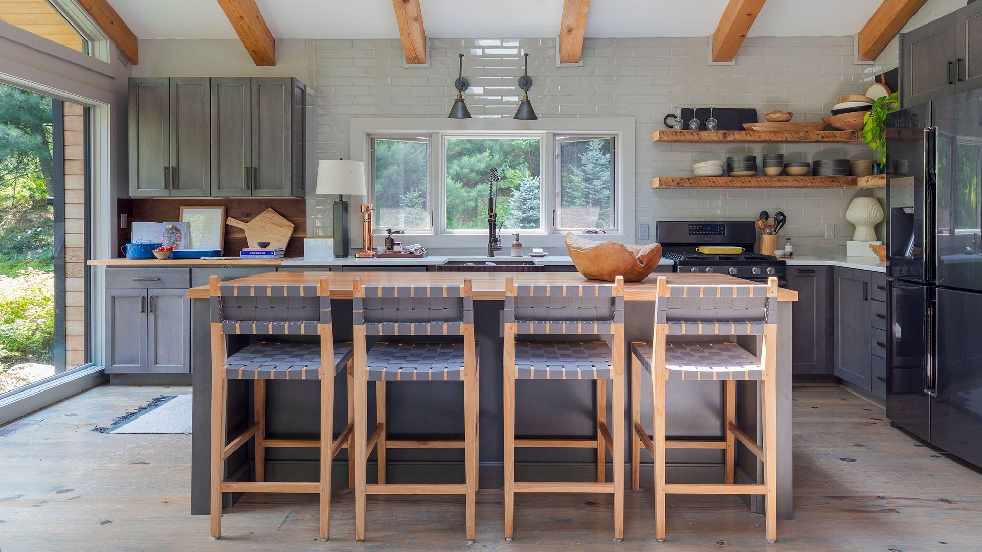 A modern kitchen with gray cabinetry, a wooden island with four stools