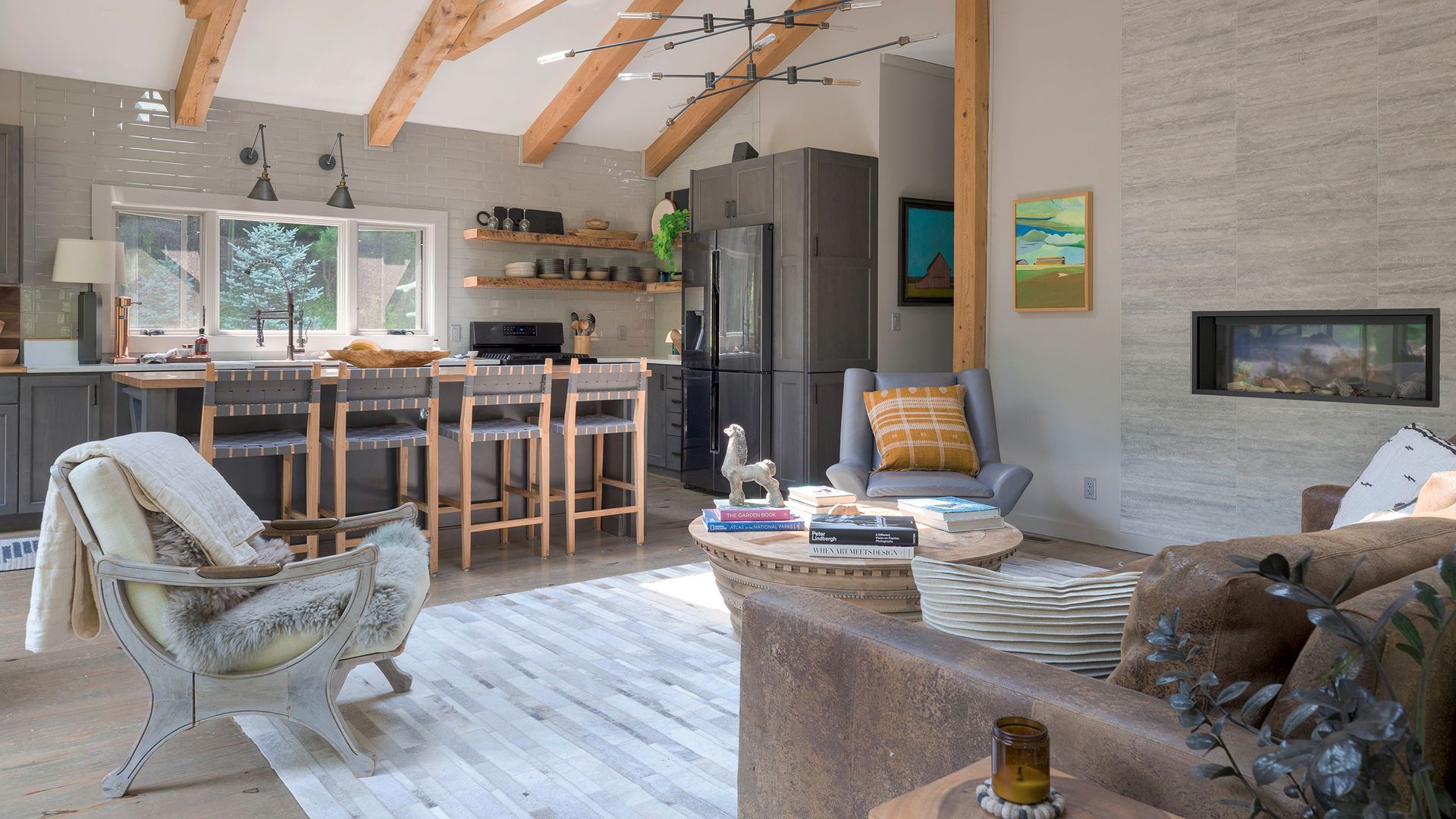 Open-plan living room with vaulted wood ceilings, a stone fireplace, kitchen island, and textured seating