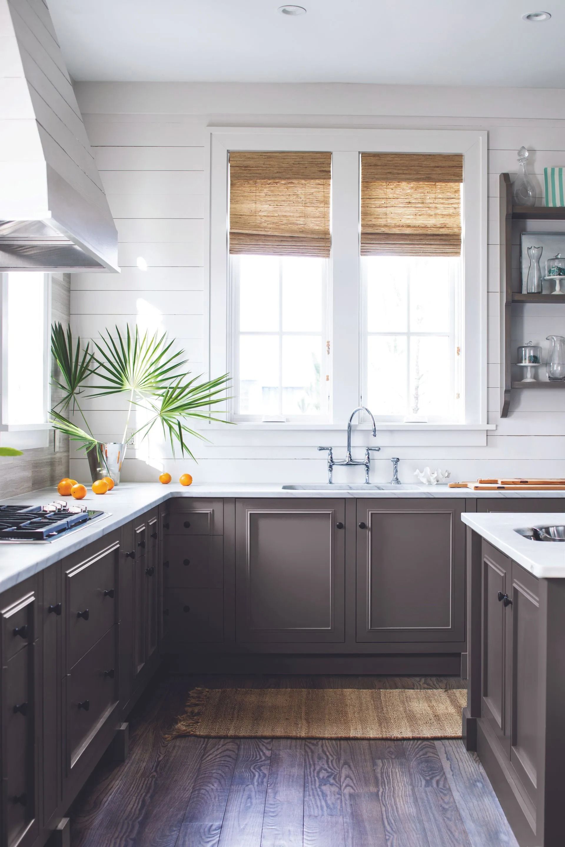 Modern kitchen with dark cabinets, white countertops, a window with woven shades, and a potted plant.