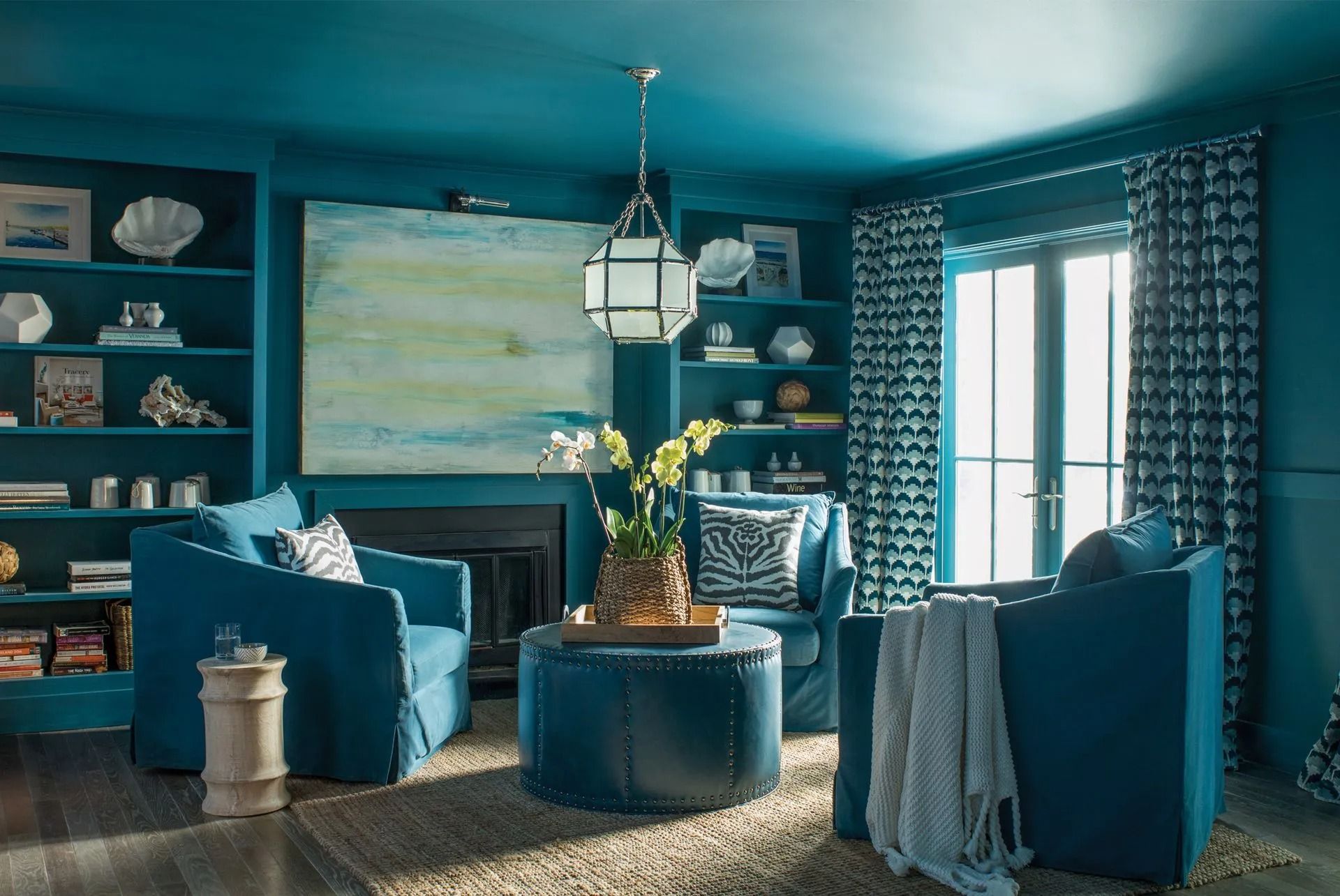 Blue living room with teal chairs, fireplace, patterned curtains, and abstract wall art