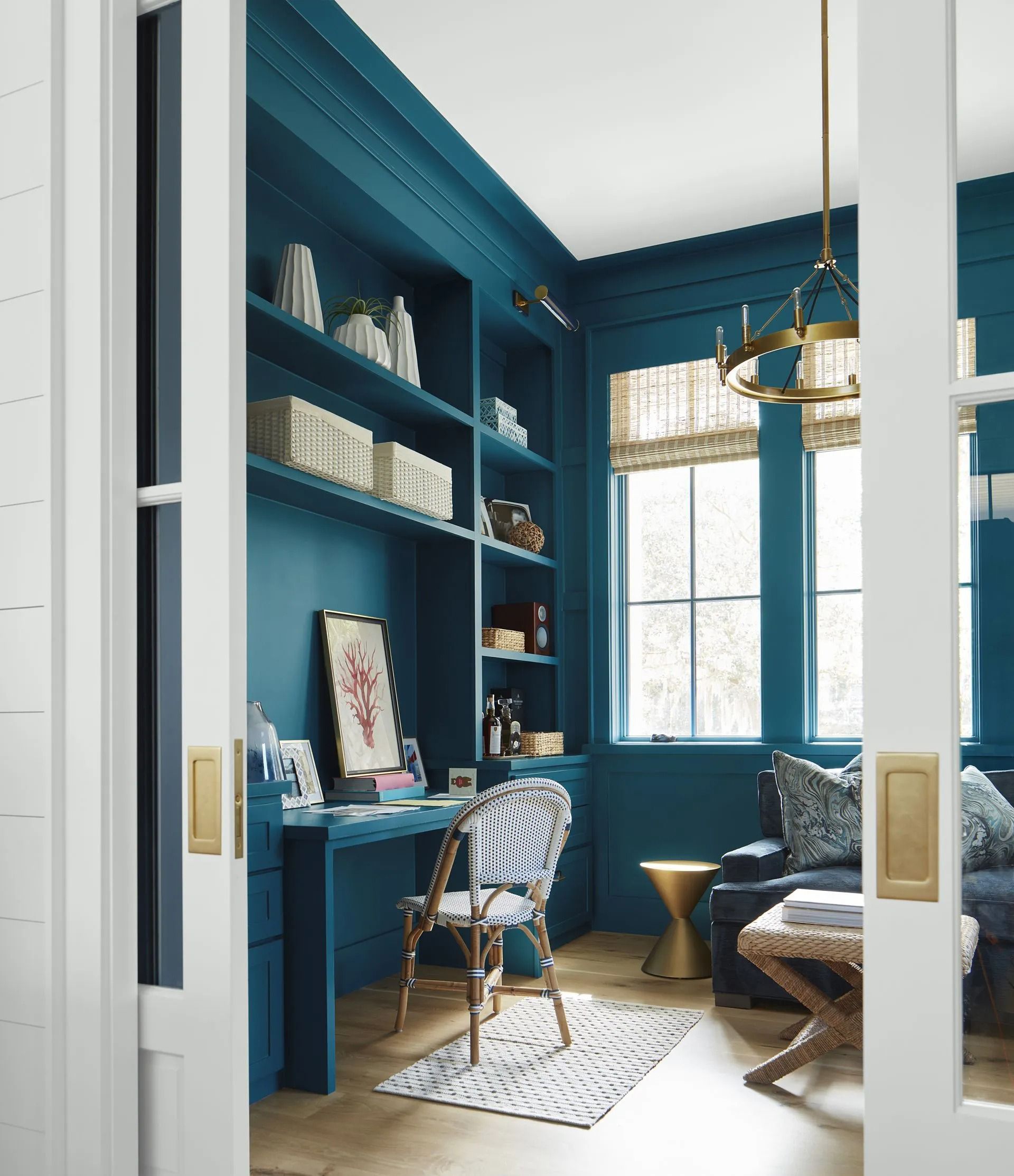Blue home office with built-in shelves, desk, chair, window, and patterned rug seen through open doors