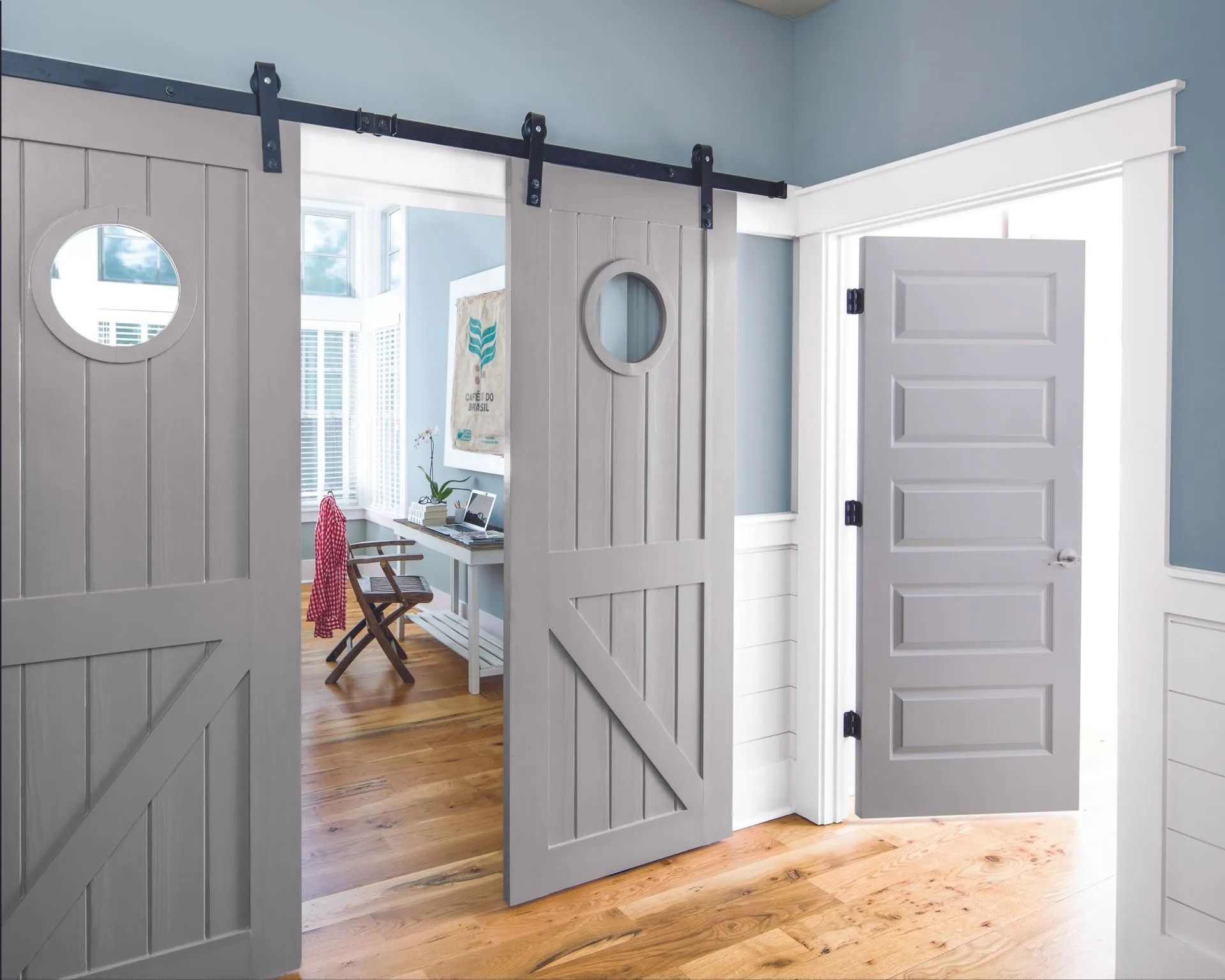 Gray sliding barn doors with round windows in a bright room with hardwood floors