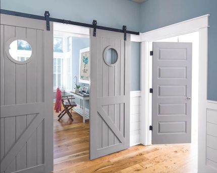 Gray sliding barn doors with round windows in a bright room with hardwood floors