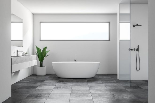 Modern white bathroom with a bathtub, plant, and glass shower. Gray tile flooring.