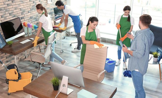 Office cleaners tidying up a modern workspace with computers, furniture, and cleaning supplies.