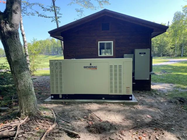A beige Generac generator installed outside a brown wooden cabin.