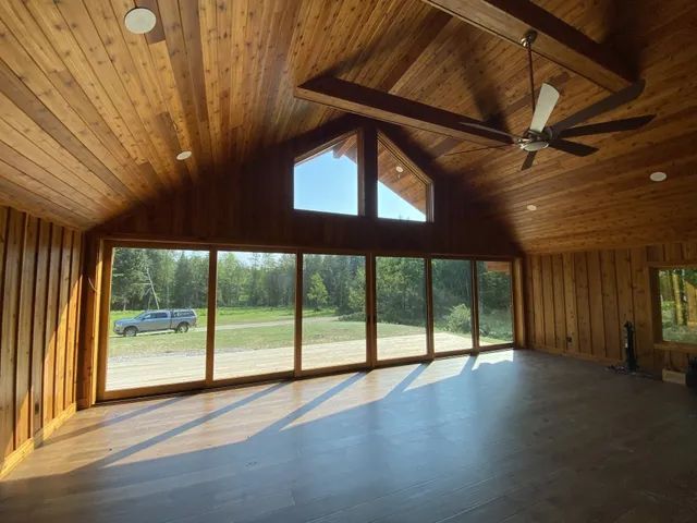 Wooden-paneled interior with large windows overlooking a field, natural light and a vehicle outside.