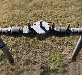 A metal backflow prevention valve assembly is installed on a pipe, positioned over a grassy lawn.