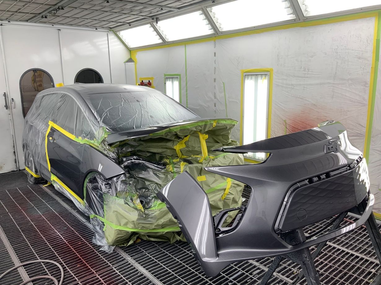 Car being painted in a paint booth; grey car with parts taped off, spray booth setting.