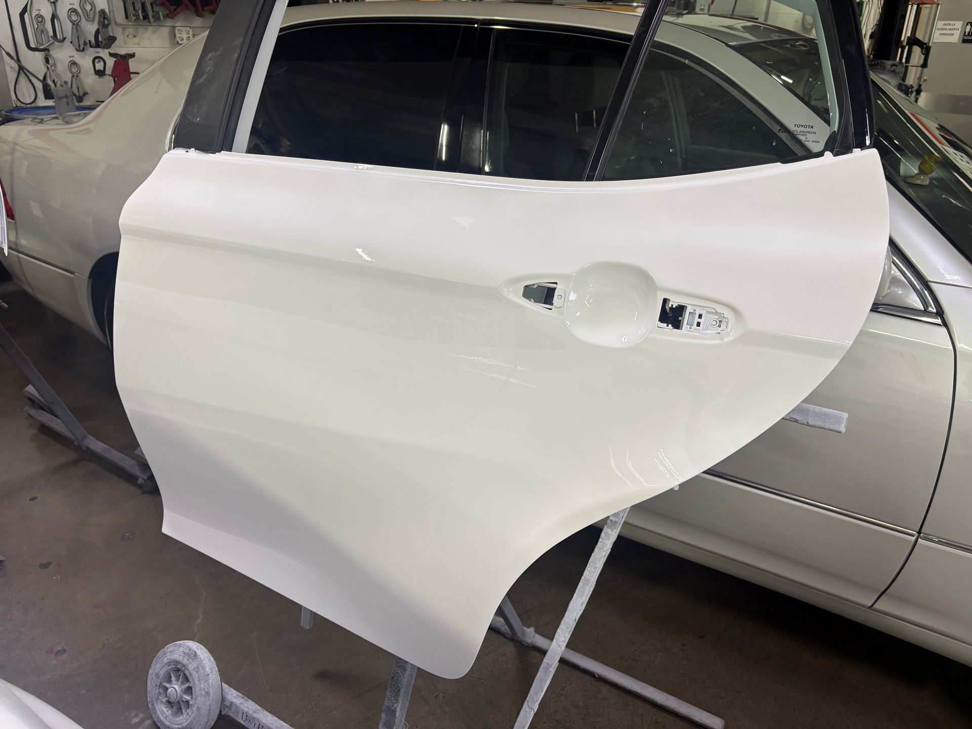 White car door panel hanging in an auto body shop, with a window and handle visible.