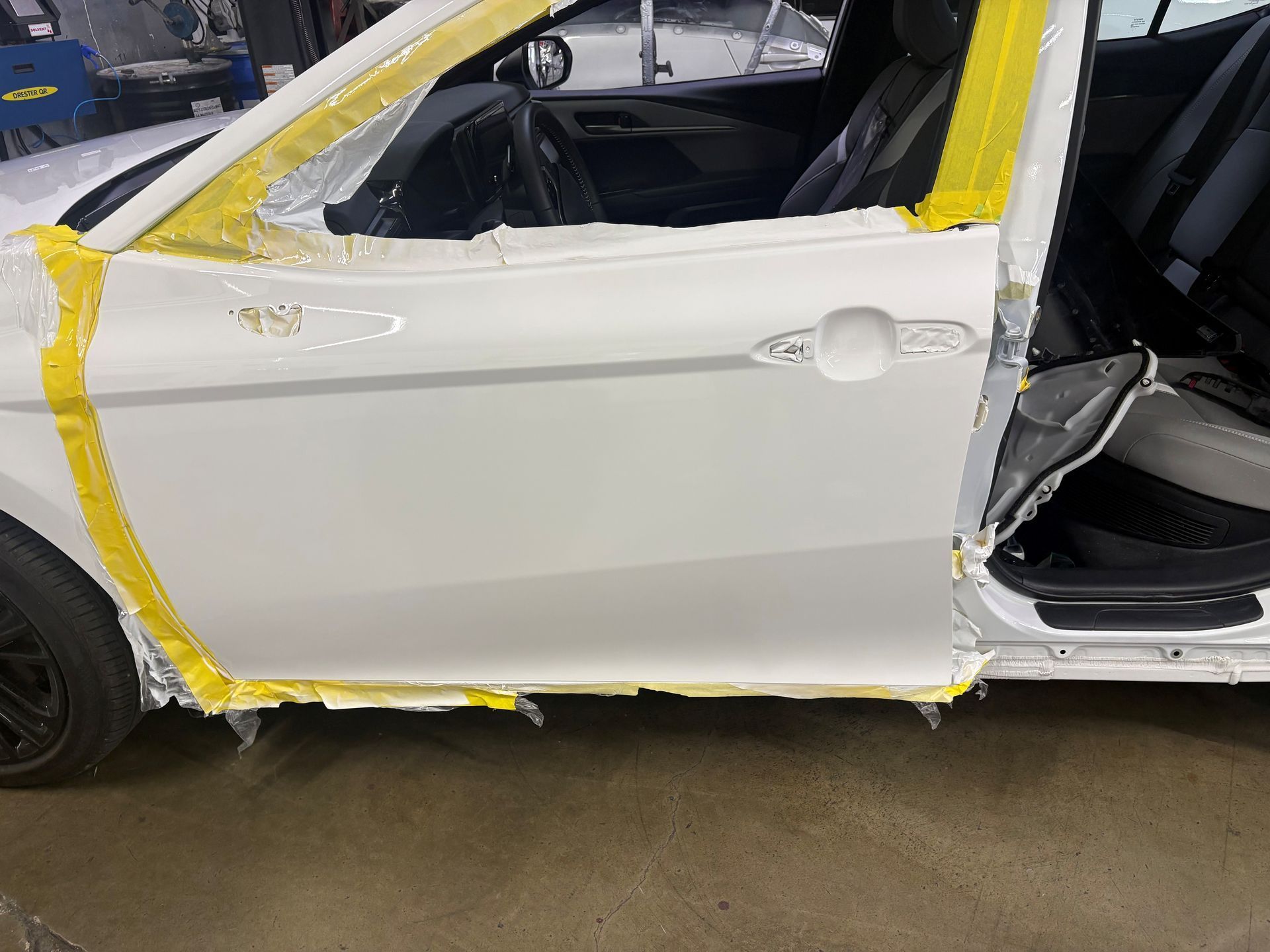 White car with side damage, yellow tape around the door and panel in a garage