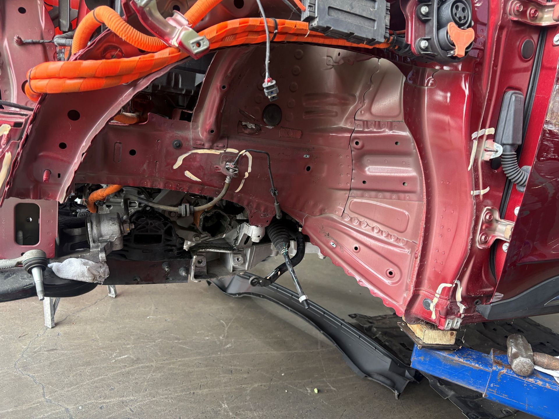 Damaged red car interior with exposed metal panels and wiring in a repair shop