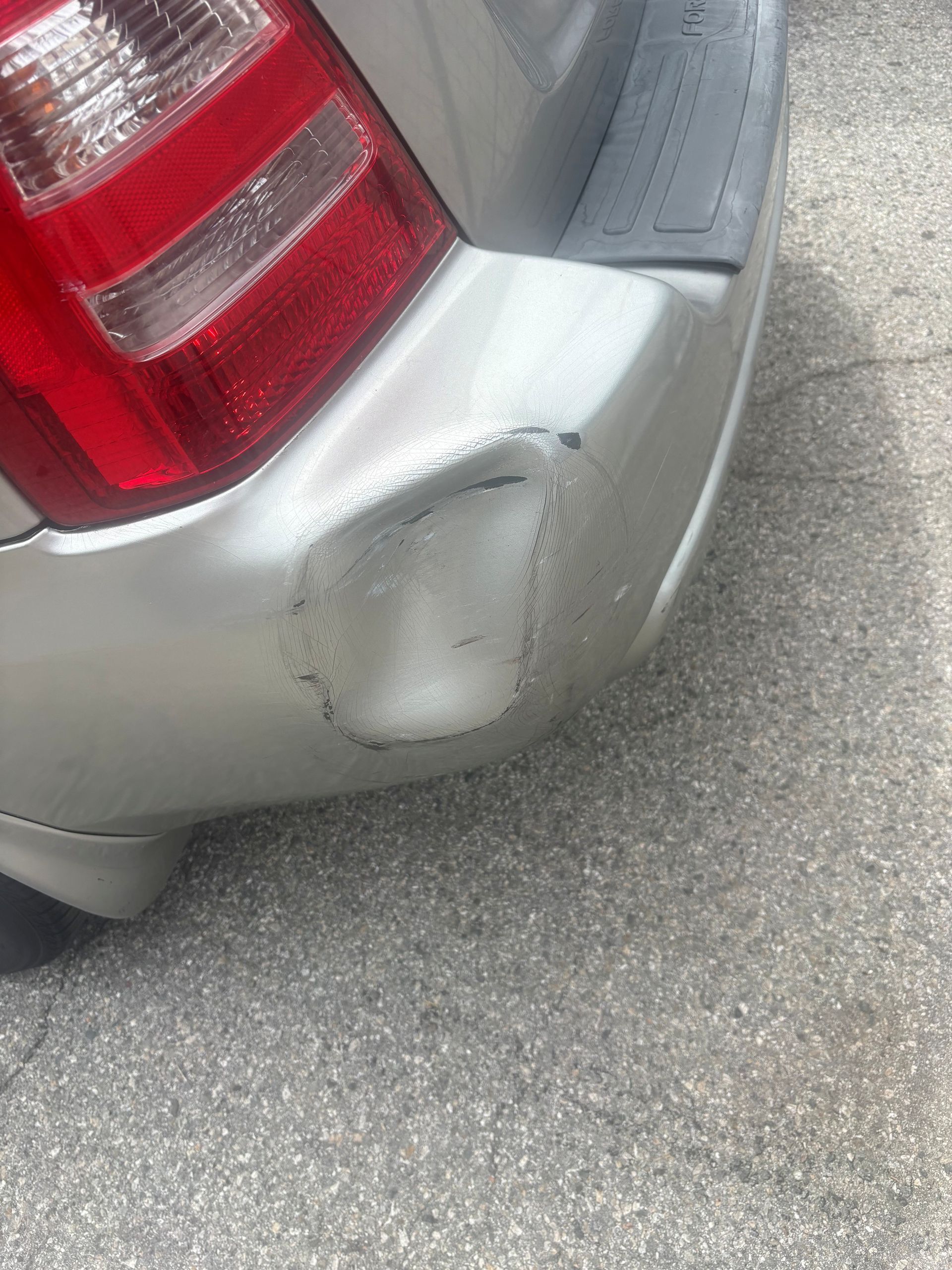 Scratched silver car bumper near red taillight on pavement