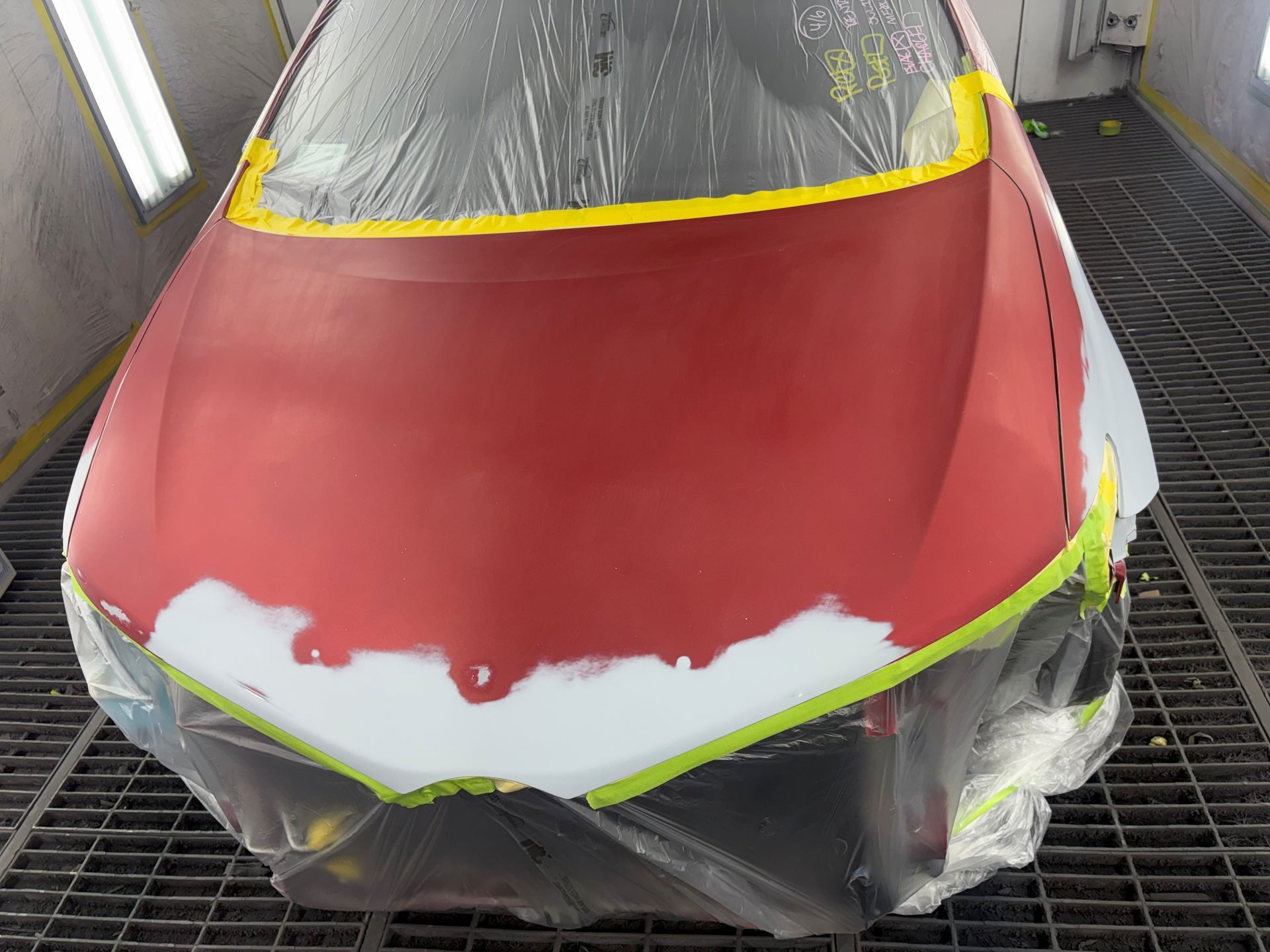 Red car hood and windshield masked for repainting in a workshop
