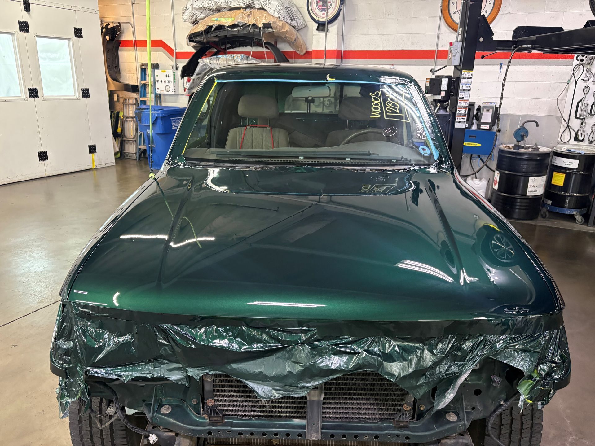 Damaged dark green classic car with a crushed front end in an auto repair shop