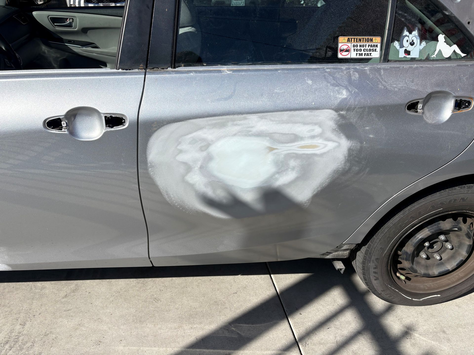 Gray car door with a large sanded paint patch and primer spot near the rear wheel