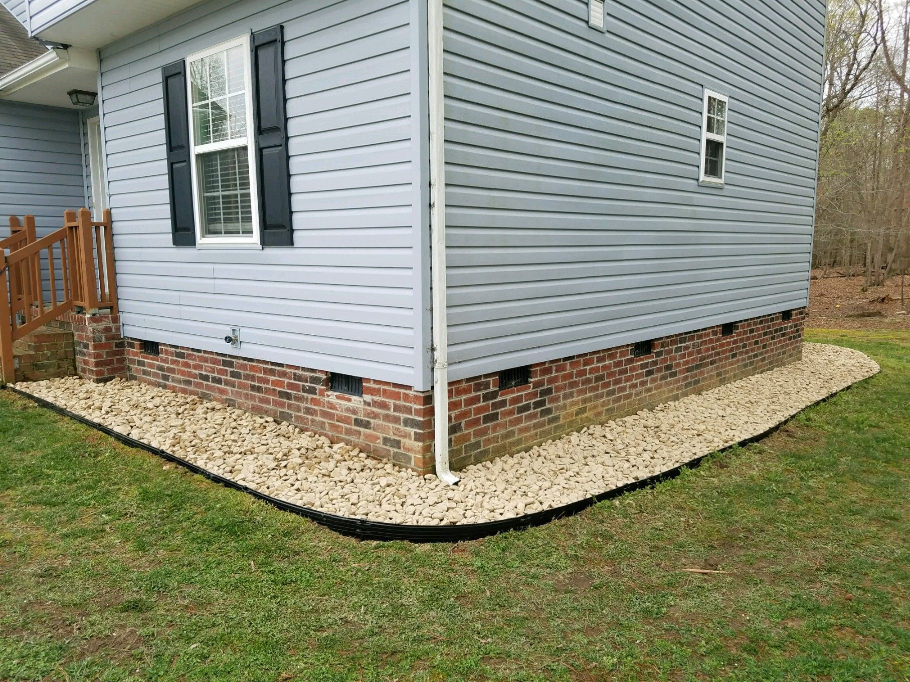 Side of a gray house with a brick foundation and gravel border along the lawn.