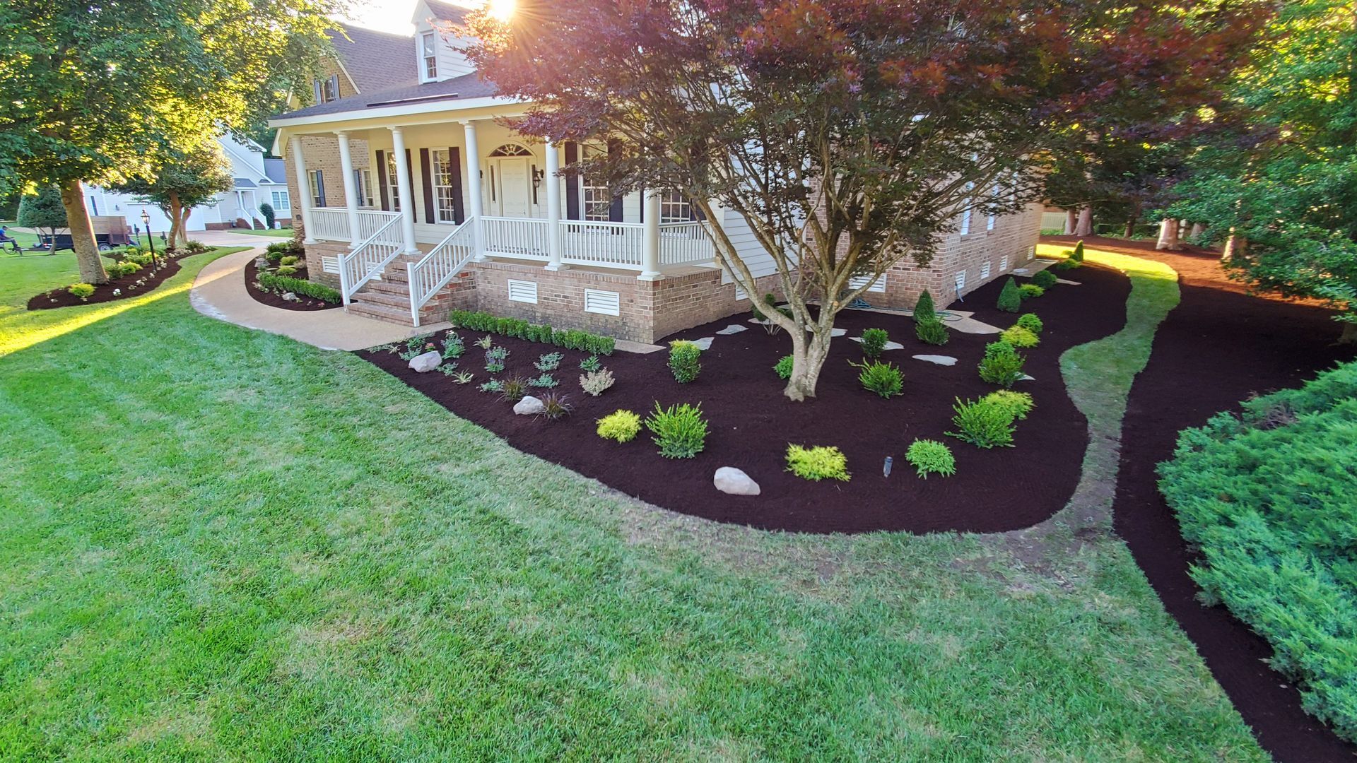 Front yard landscaping with fresh mulch, small shrubs, and a porch beside a green lawn.