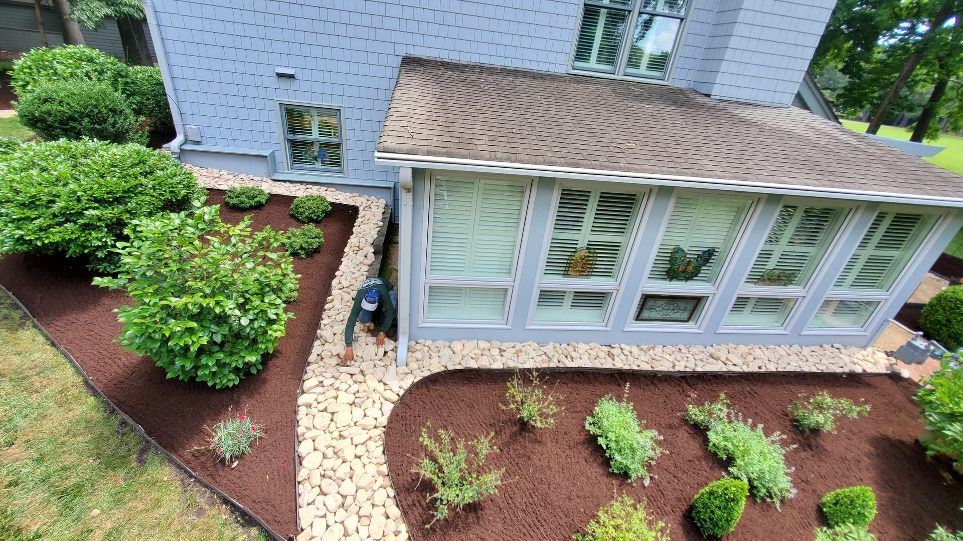 House exterior with curved brick path, green shrubs, and a screened porch surrounded by mulch beds