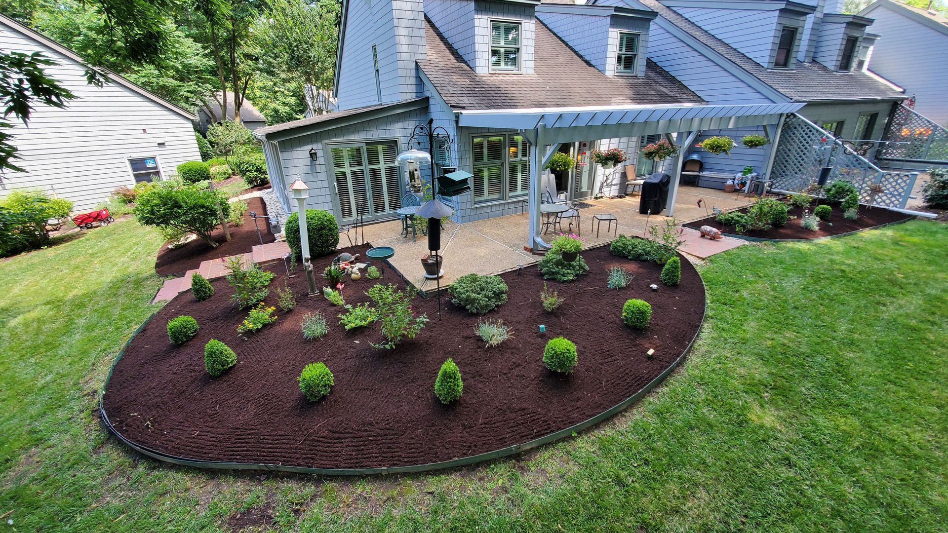 Front yard landscaping with new shrubs in a mulched garden bed beside a house and patio.