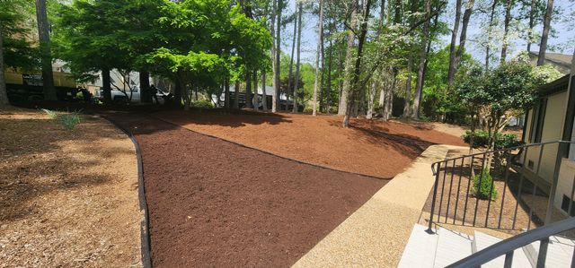 Landscaped garden with mulch beds, trees, and a concrete walkway beside a patio.