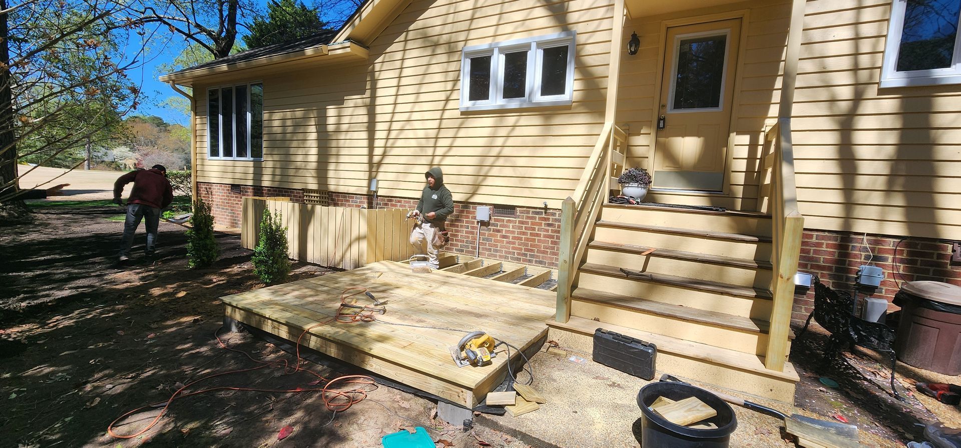 Yellow house exterior with small steps, stone path, and a person by a tree in the yard