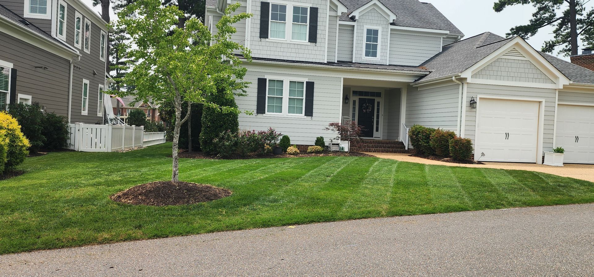 Suburban townhouse with white shutters, attached garage, and a green lawn along a paved street