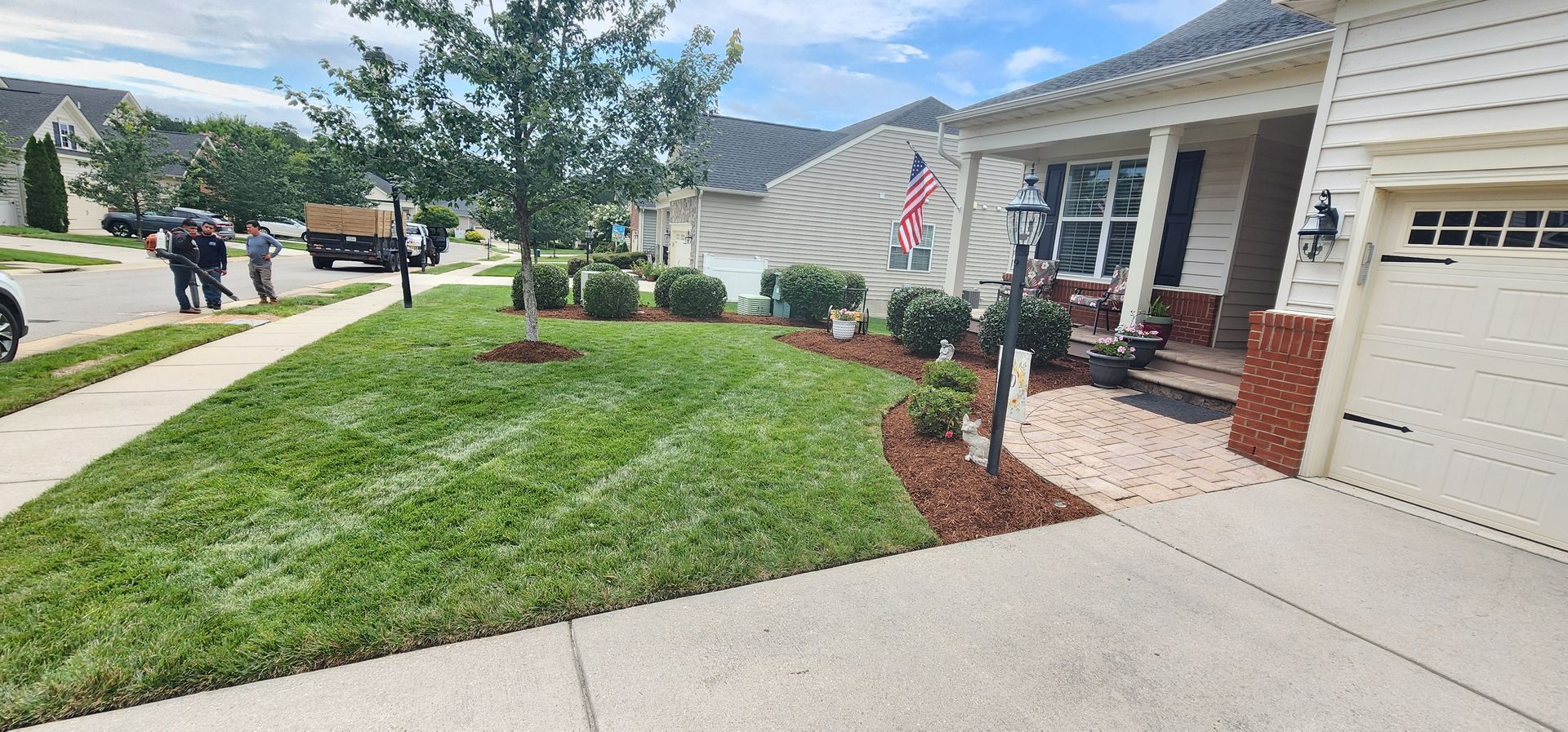 Suburban house with manicured lawn, brick porch, and American flag along a curved sidewalk