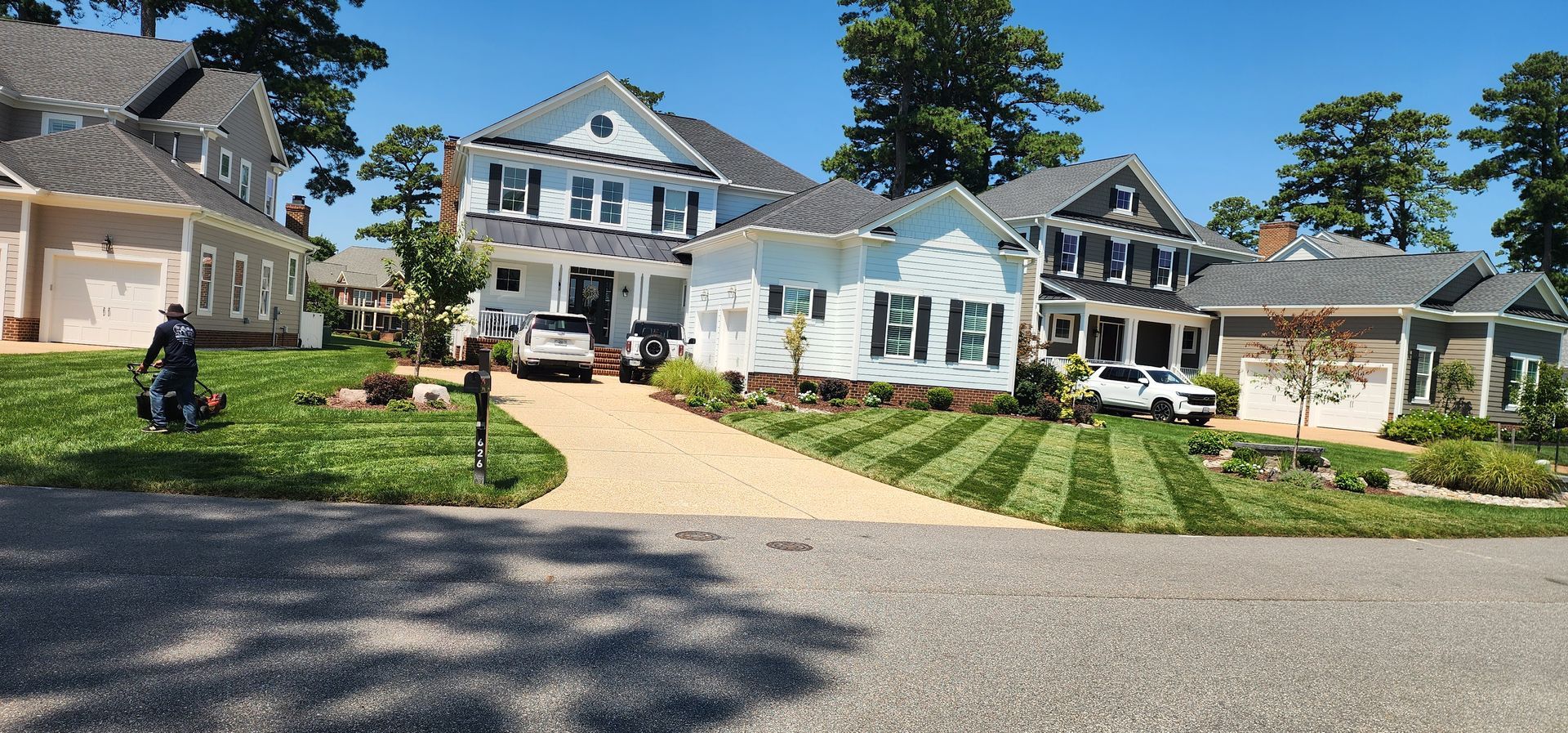 Row of houses with a white home centered, a driveway, and a parked motorcycle in a sunny neighborhood
