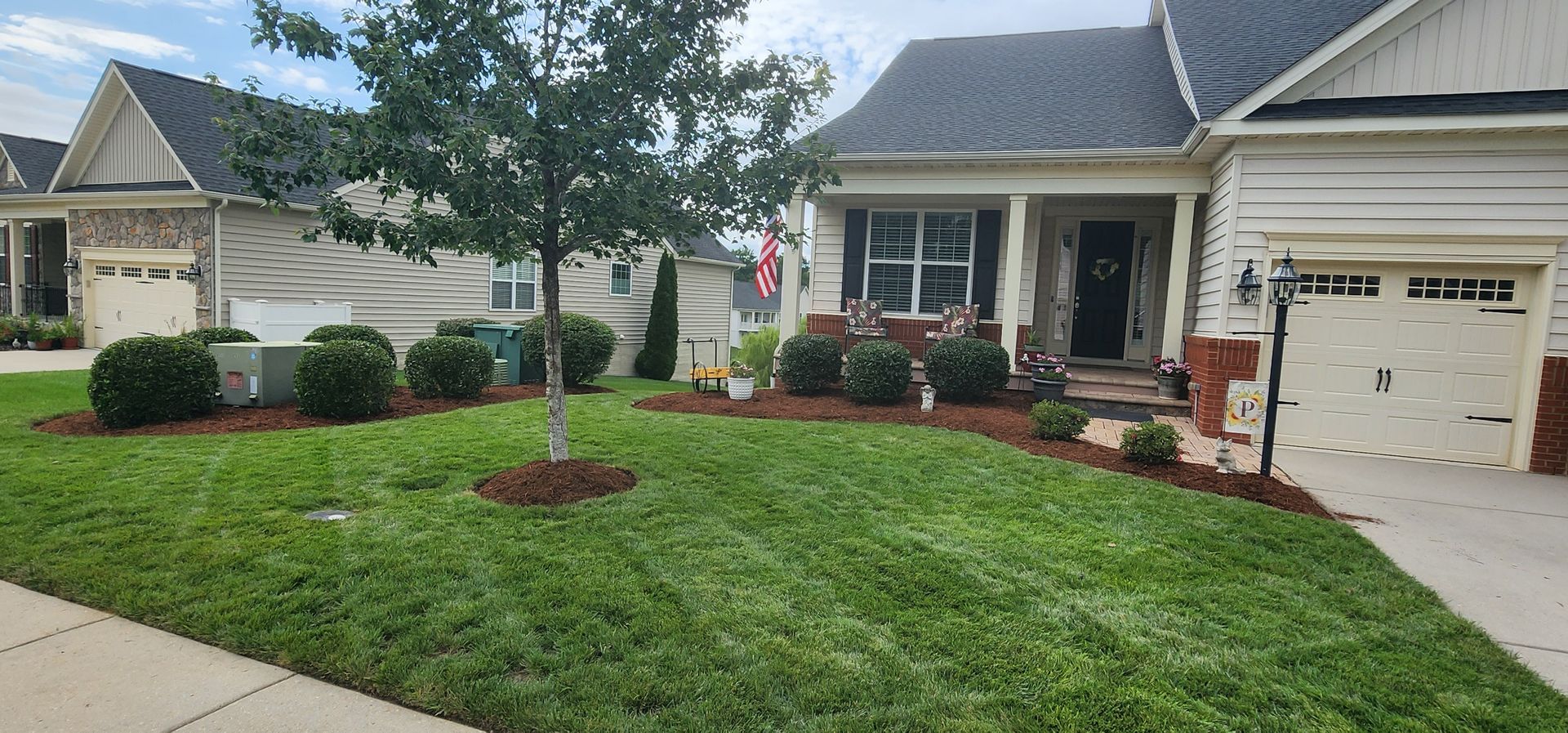 Suburban house with a manicured lawn, trees, shrubs, and a garage driveway