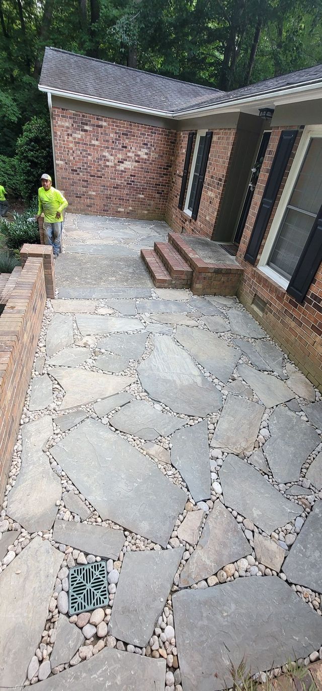 Stone patio with brick house and a person in a neon safety shirt near the edge of the walkway
