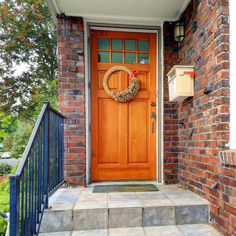 The front door of a brick house with an orange door and a wreath on it.