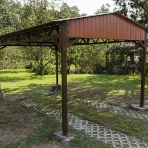 A wooden gazebo with a red roof is sitting in the middle of a grassy field.